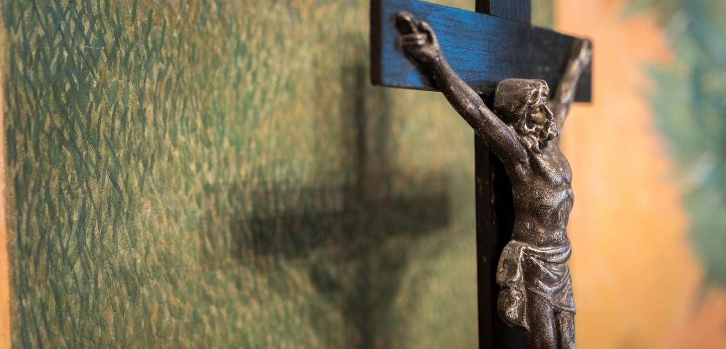 Jesus on the cross pictured close to a green wall. 