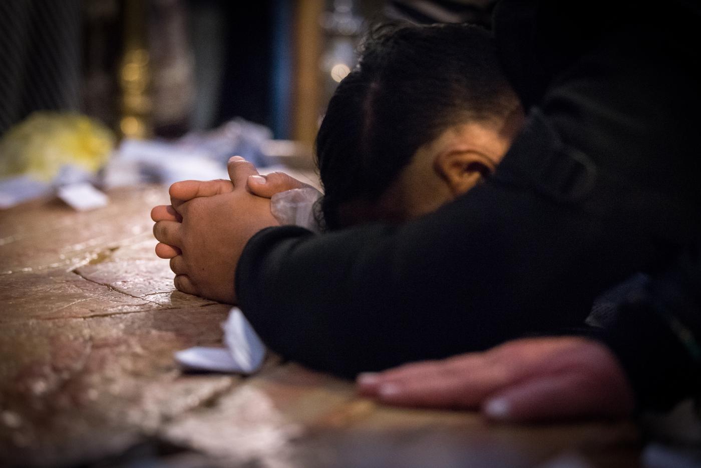A man prays with his hands clasped and face burried in his arms, on the Stone of Anointing.
