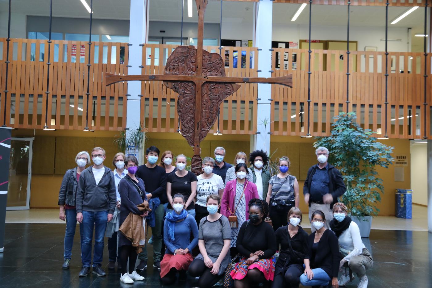 Group posing for a group photo in fronto of a wooden cross, wearing face masks