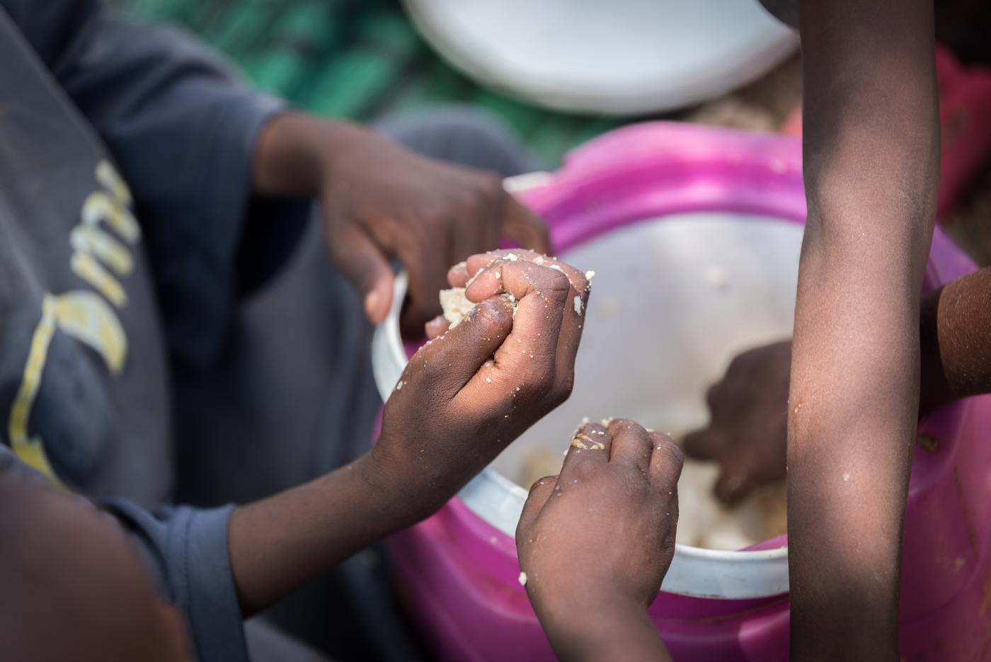 Children's hands seen grabbing hold of food from a pink plastic bowl. 