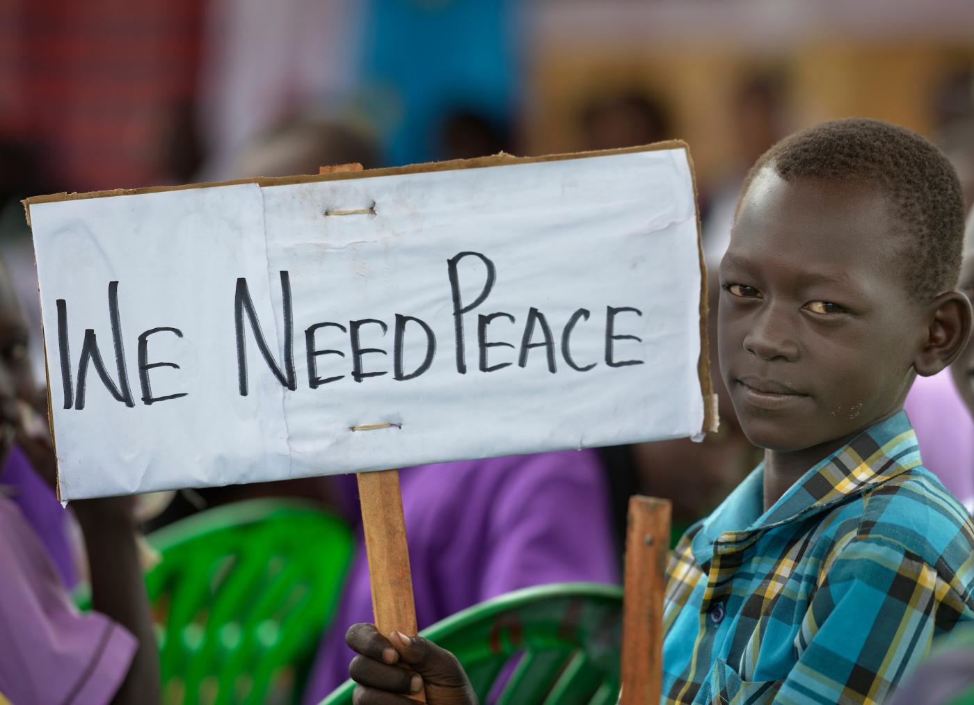 African boy looking into the camera holds a sign saying "We need peace". 