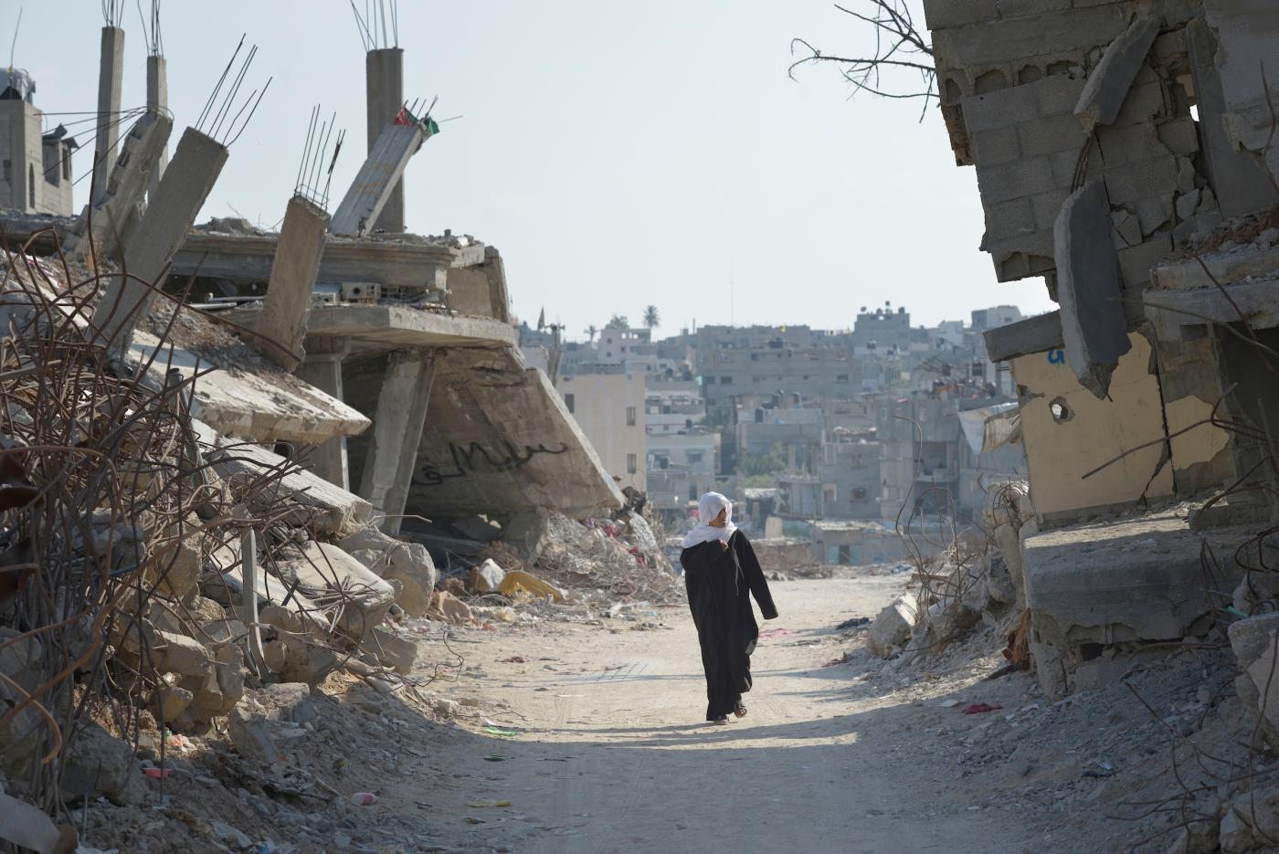Woman walks amidst demolished buildings
