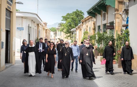 A group of people, many of which are wearing religious garb, walk in an old town setting on a sunny day. 