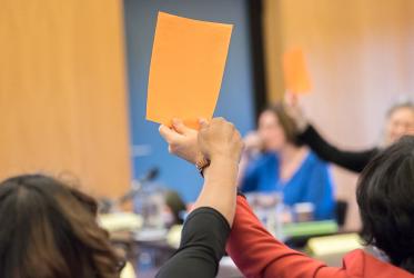 People hold orange paper cards up in the air as a symbol of consensus, affirmation, during a World Council of Churches meeting.