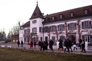 People walking in front of large white building in the countryside. 