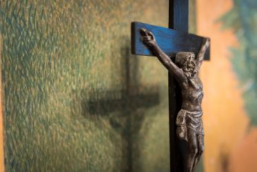 Jesus on the cross pictured close to a green wall. 
