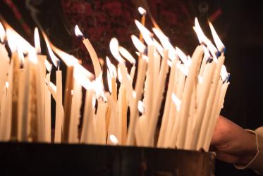 Many candles seen against dark background. 